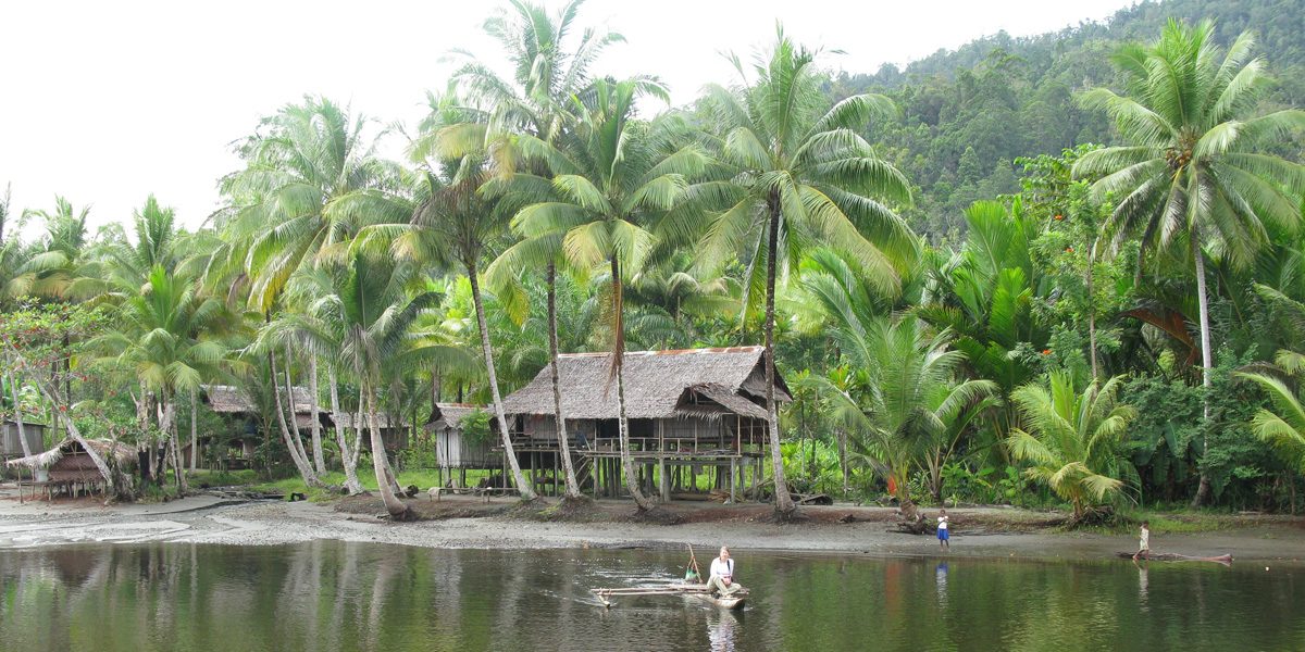 Woman on a boat in front of a backdrop of trees and village huts