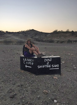 Anthropology student sitting on a sign for photo