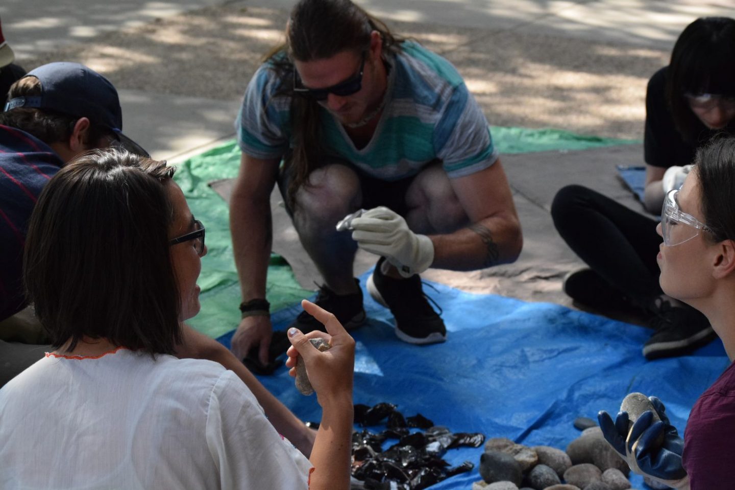 Group wearing goggles and glasses doing flintknapping activity on tarp