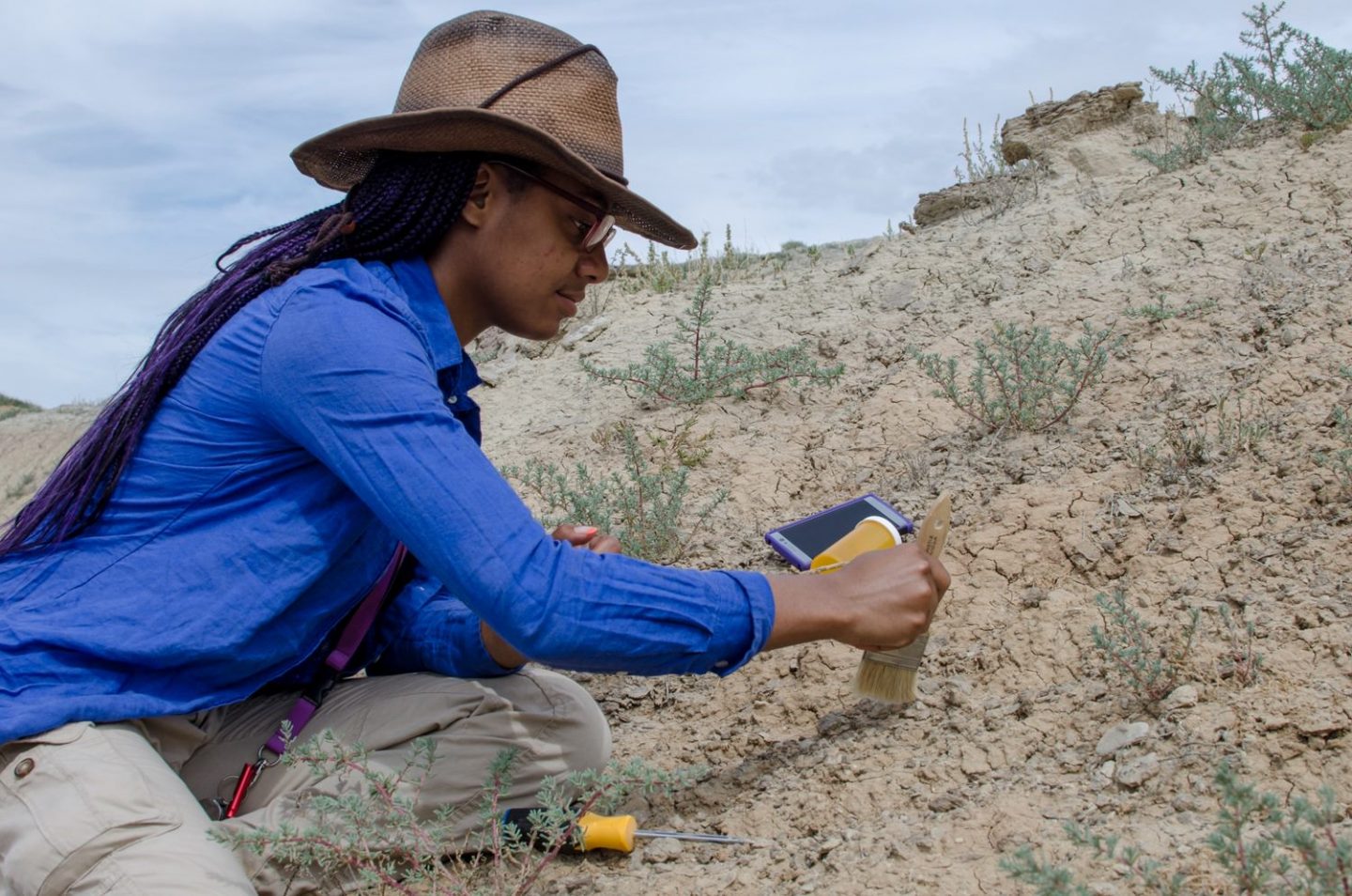 Student using brush in the dirt during Paleontology Field School