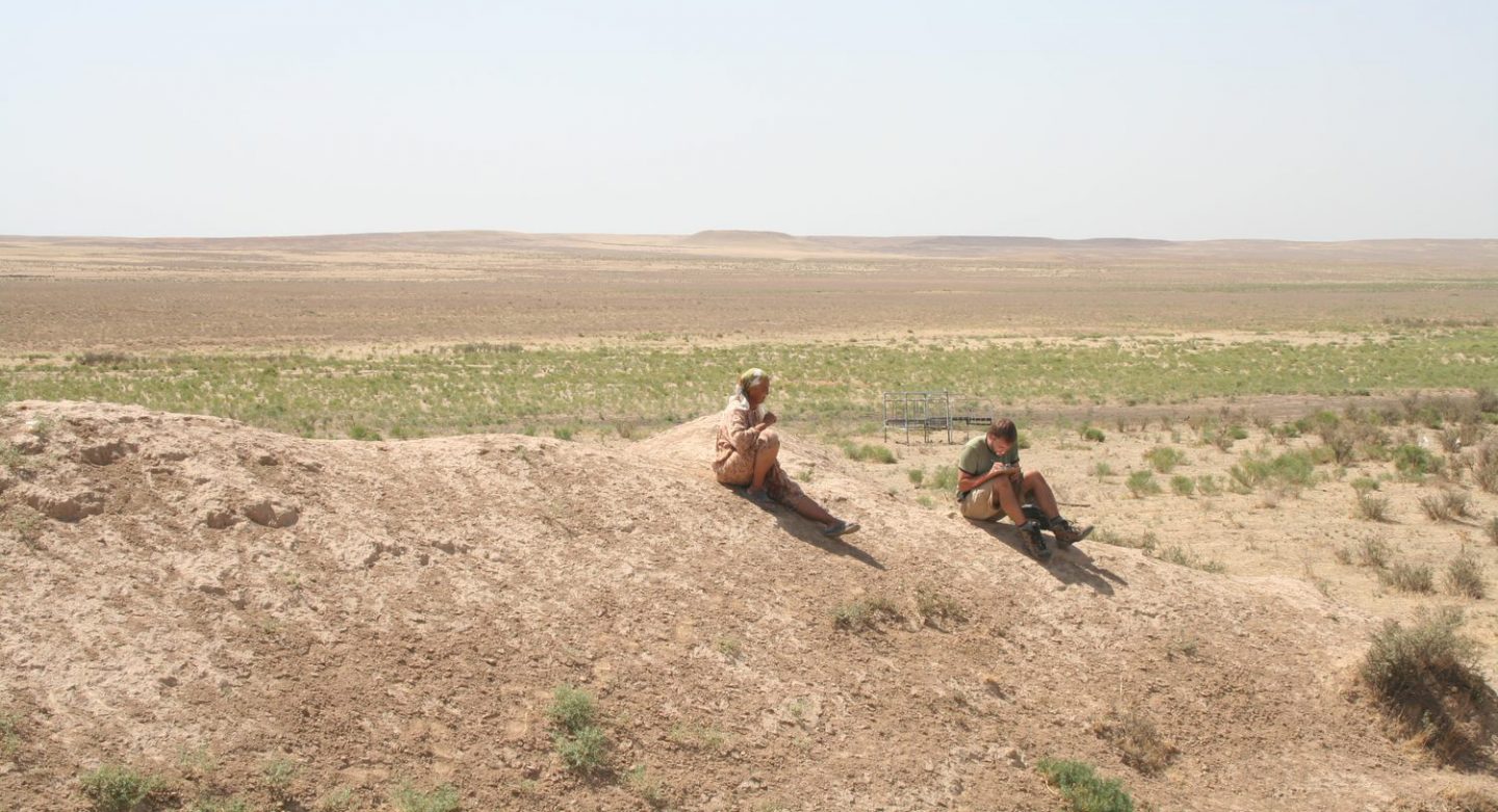 Two people working in the field, sitting on a dirt mound