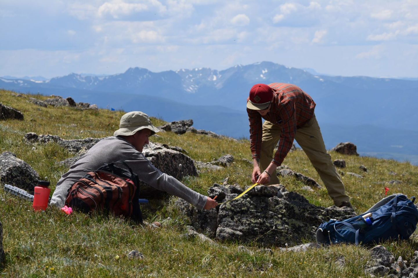 Two students using a tape measure on a rock in a field