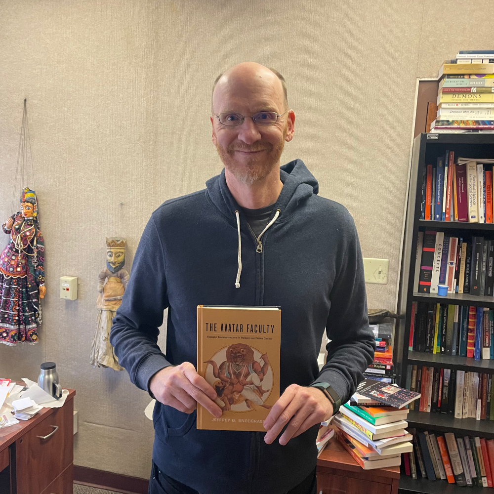 Professor with hoodie sweatshirt holding book The Avatar Faculty