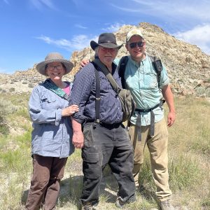 Female professor in sun hat, male professor in cowboy hat, and male professor in baseball cap in front of badlands