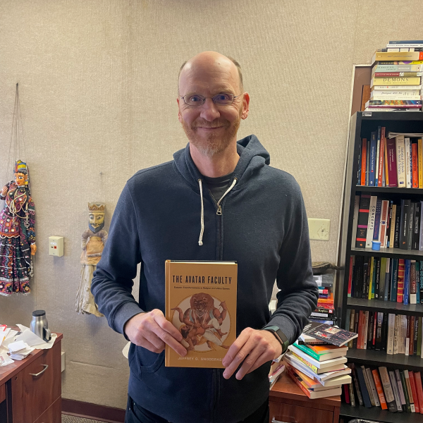Professor wearing hoodie sweatshirt holding copy of book
