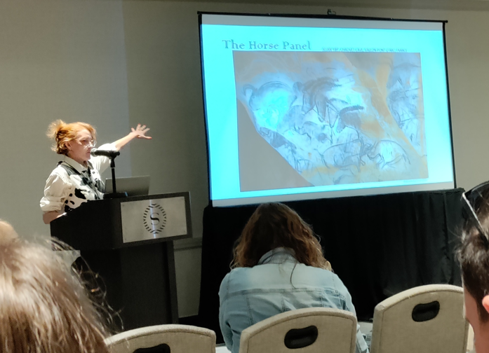 image of student standing and pointing at screen durign conference presentation.