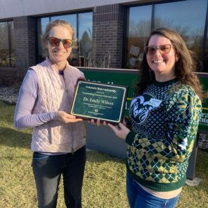 Two people standing outdoors holding an award plaque