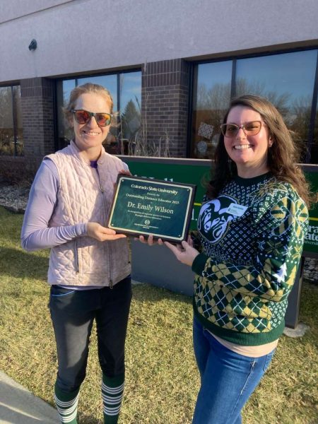 Two people standing outdoors holding an award plaque