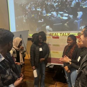 Students from the "Real Talk" URA chatting in a circle in front of a poster at MURALS