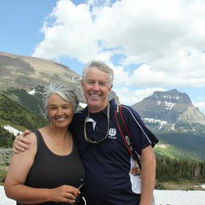 Susan Harness and her husband Rick smile in front of a mountain range