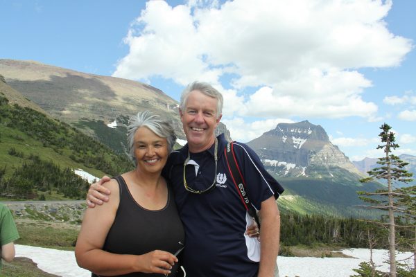 Susan Harness and her husband Rick smile in front of a mountain range
