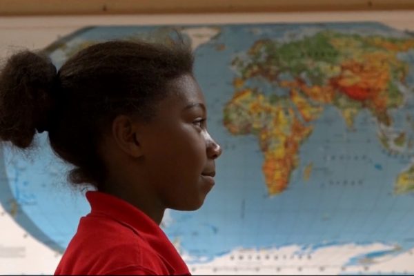 School-aged girl standing in a classroom in front of a world map