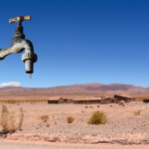 A faucet drips in front of an arid landscape
