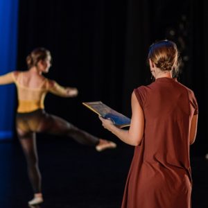 Dancer practices while teacher takes notes on form
