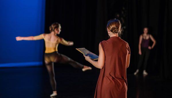 Dancer practices while teacher takes notes on form