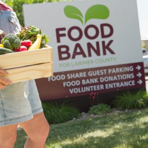 Woman carrying a box of fresh produce in front of the Larimer County Food Bank