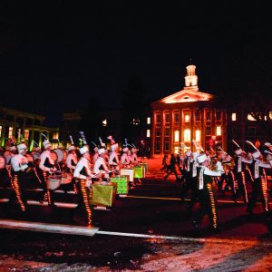 Marching band pictured in front of the University Center for the Arts at night