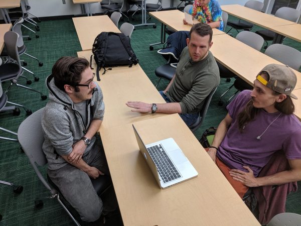 three students talking at a table in a classroom