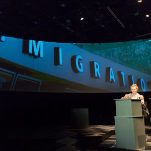 An actress in front of a backdrop that says "Immigration"