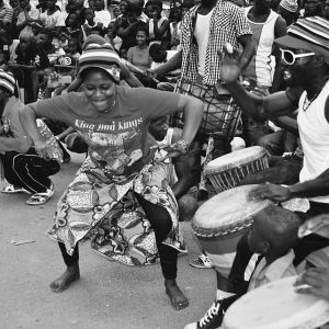 A woman pumping her arms and dancing dundunba on a street as a man plays a djembe drum, Conakry, Guinea