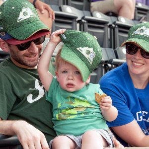 Two adults and a child smiling in the stands at the 2022 Rams at the Rockies baseball game.
