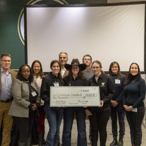 A group of College students and faculty stand in front of a screen, holding a large check for the amount of $4,000 in prize winnings.
