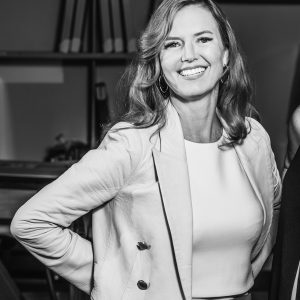 Martha McGee smiling and looking at camera wearing an open jacket, hand on hip