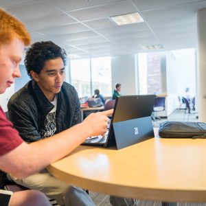 Two students huddle over a shared laptop while studying at the library