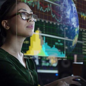 Woman wearing glasses examines a computer screen with transposed images of world markets and data in front of her