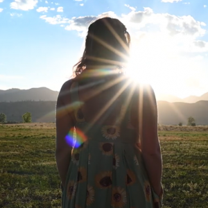 Woman in dress stands and looks at the setting sun