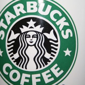 A closeup shot of a white coffee mug with the green and black Starbucks logo on it