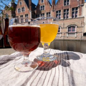 Tasting of Belgian beer on open cafe or bistro terrace with view on medieval houses and canals in Bruges, Belgium in sunny day