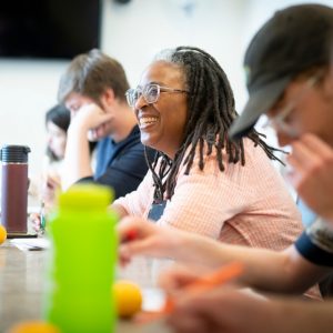 Woman smiles as she sits between several students at a table
