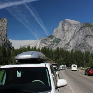 Cars parked along each side of the road with evergreen trees and mountains in the background