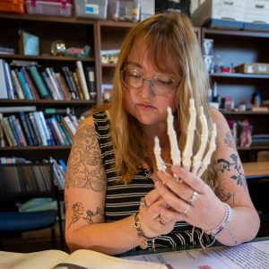 Student examines a skeletal hand model alongside anatomy reference materials.