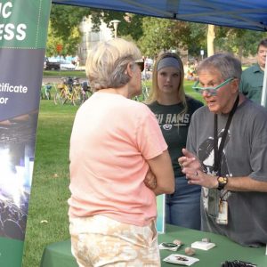 A man talks with a person at a booth with a sign next to it advertising the Music Business Program